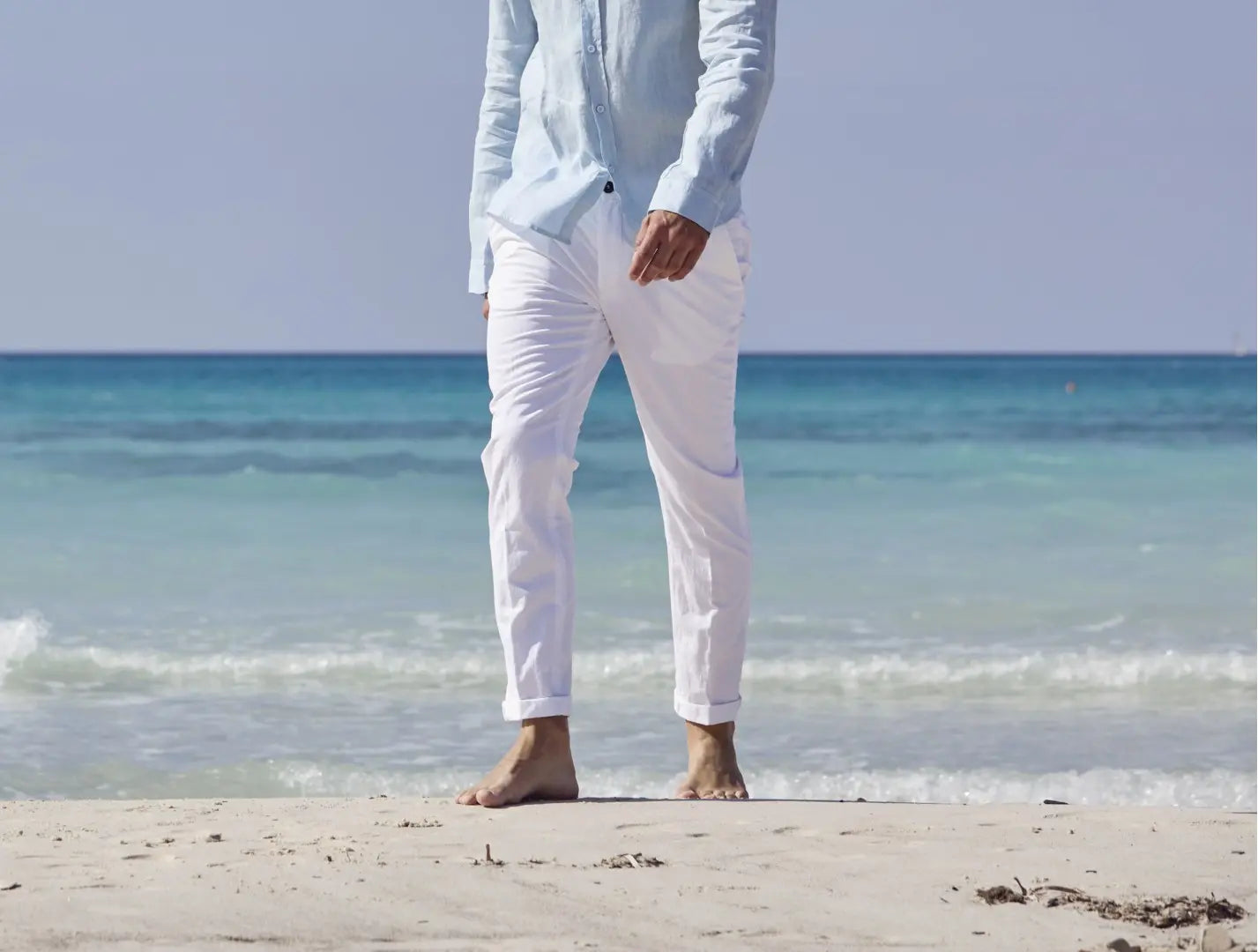 primo piano pantaloni bianchi di un ragazzo che passeggia in riva al mare